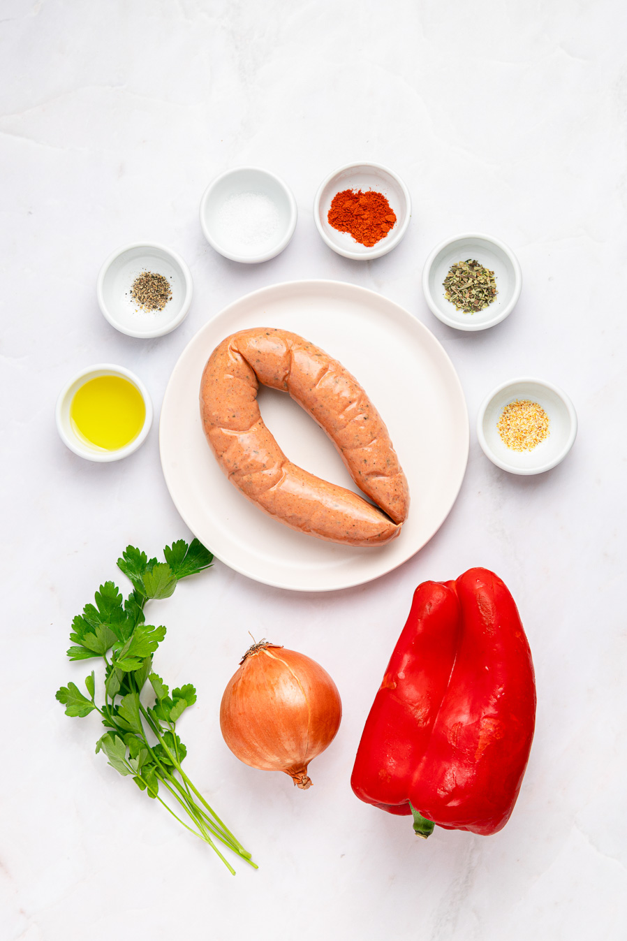 Air fryer kielbasa, red bell pepper, onion, parsley, oil, and spices are artfully arranged on a white surface.