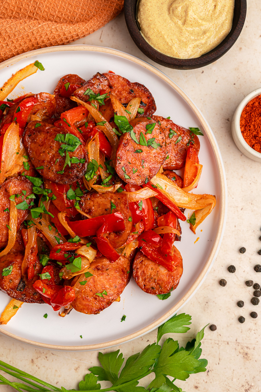 Sliced air fryer kielbasa with saut&eacute;ed onions and red peppers on a plate, garnished with parsley. Mustard on the side.