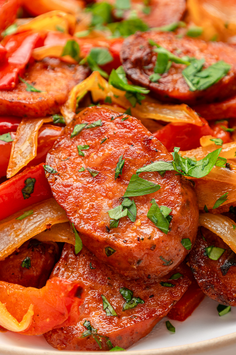 Sliced air fryer kielbasa with cooked red and yellow peppers, onions, and fresh parsley on a white plate.