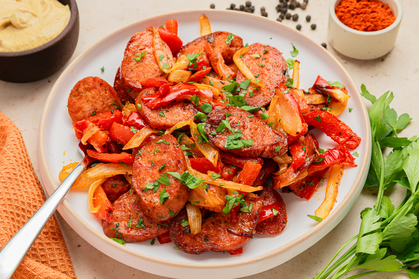 Sliced air fryer kielbasa with saut&eacute;ed peppers, onions, and herbs on a white plate with a fork.
