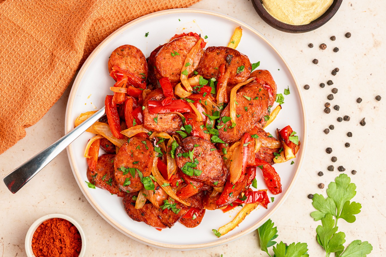 A plate of saut&eacute;ed sausage with red bell peppers, onions, and herbs&mdash;featuring air fryer kielbasa&mdash;garnished with chopped parsley.