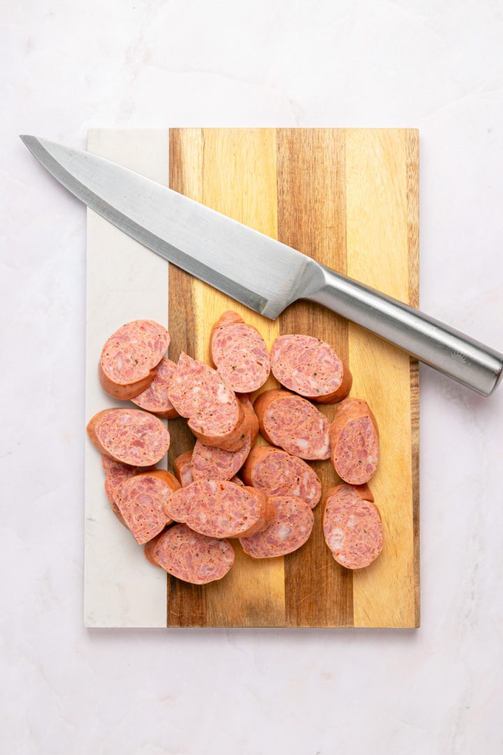 Slices of air fryer kielbasa on a small cutting board with a large kitchen knife beside them.