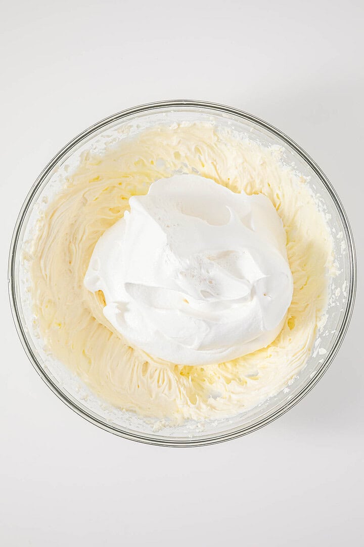 A glass bowl with whipped cream and meringue on a white background, seen from above—a delightful nod to the vintage Cherries in the Snow Dessert.