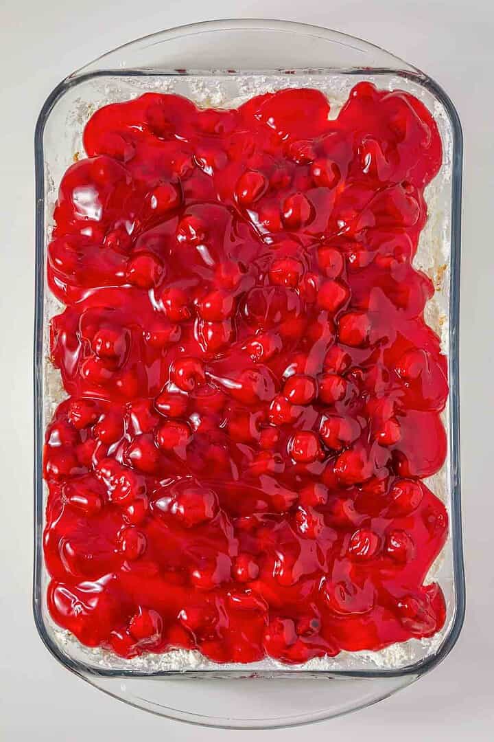 Rectangular glass dish filled with bright red cherry pie filling on top of a dessert, reminiscent of the vintage Cherries in the Snow Dessert.