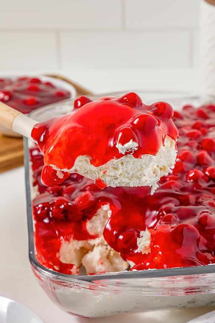 A spoon scoops a serving of the vintage Cherries in the Snow Dessert, topped with luscious cherries, from a glass baking dish.