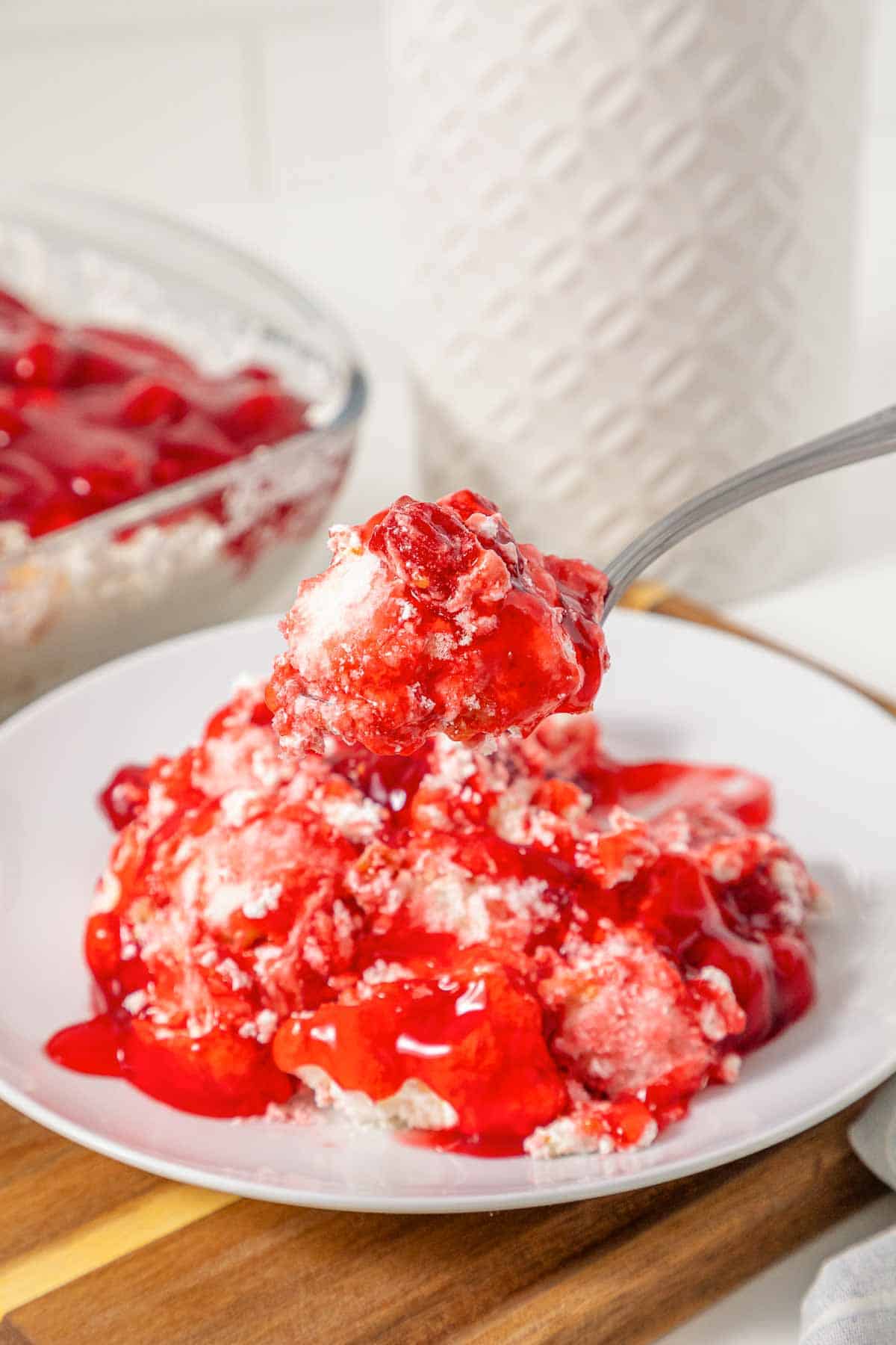 A fork holds a bite of vintage Cherries in the Snow Dessert over a plate with more cherry and cream dessert.