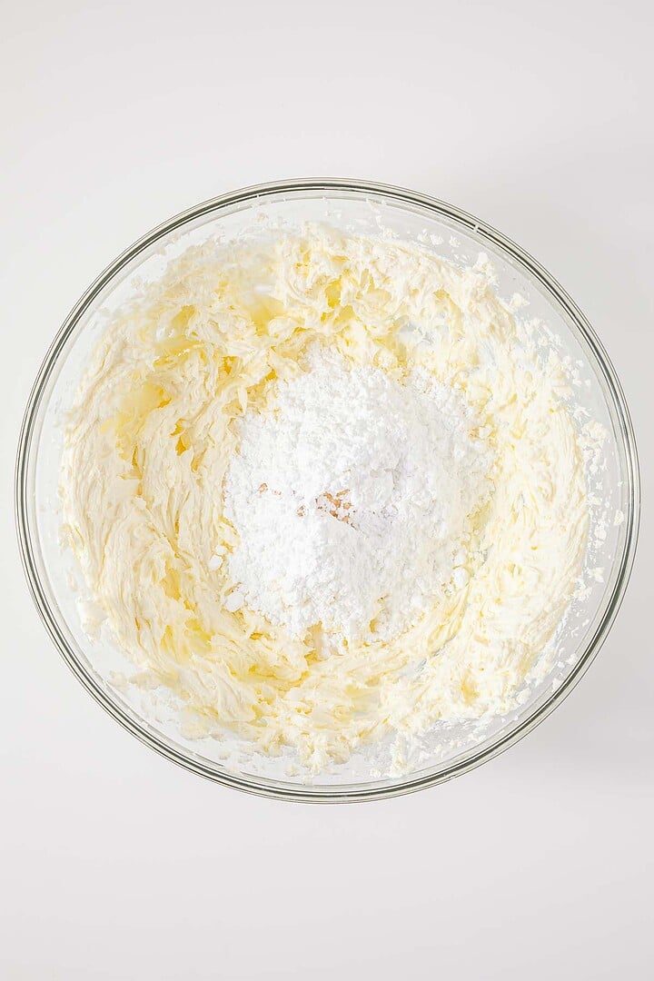 A glass bowl with whipped butter and powdered sugar being mixed together on a white surface, just as you would when preparing the classic vintage Cherries in the Snow Dessert.