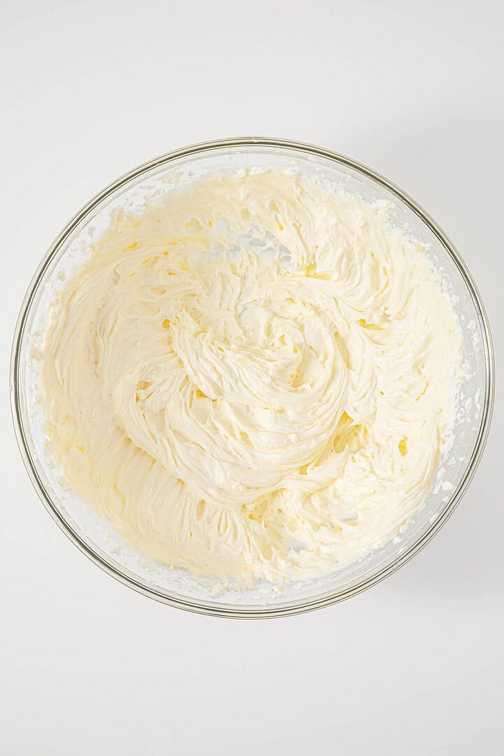 A glass bowl filled with whipped cream or frosting, viewed from above on a white background, evokes the timeless charm of a vintage Cherries in the Snow Dessert.