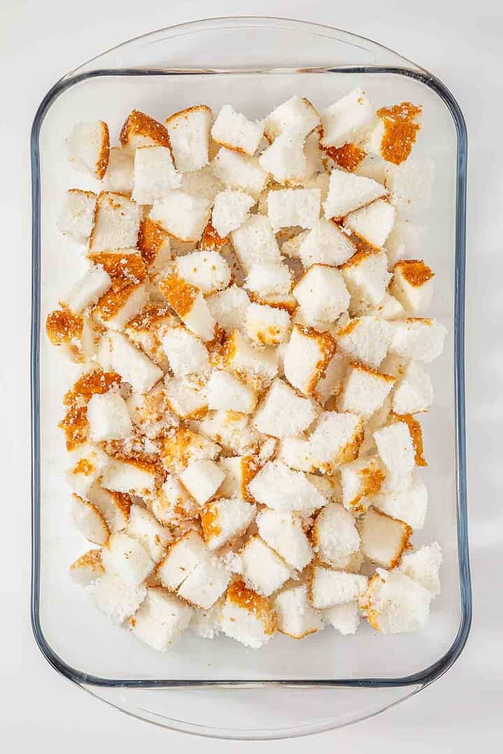 Cubed pieces of bread spread evenly in a glass baking dish, ready for baking or further preparation—an essential first step in crafting a vintage Cherries in the Snow Dessert.