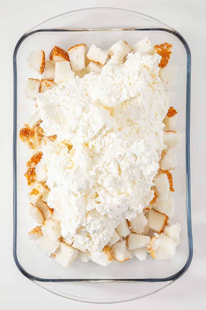 Cubed angel food cake in a glass dish topped with a large mound of whipped cream mixture creates a delightful presentation reminiscent of the vintage Cherries in the Snow Dessert.