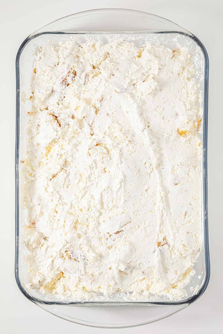 A glass dish filled with a layer of fluffy whipped cream spread evenly over a vintage Cherries in the Snow Dessert.
