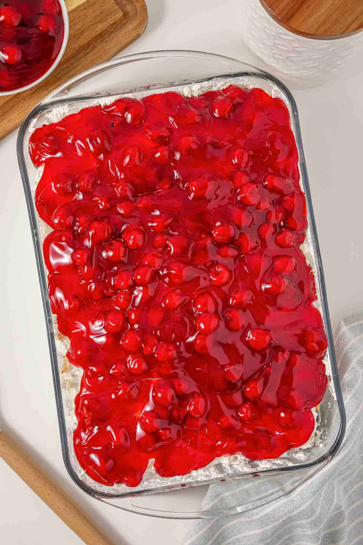 Rectangular dish filled with bright red cherry pie filling on a creamy dessert base, reminiscent of the vintage Cherries in the Snow Dessert.