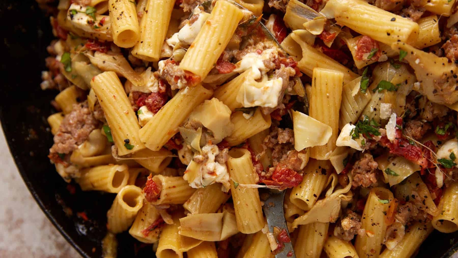 Rigatoni pasta with ground meat, artichokes, sun-dried tomatoes, herbs, and melted cheese mixed together.