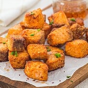 Crispy golden tofu cubes garnished with chopped chives on parchment paper, reminiscent of the delicious texture found in Air Fryer Parmesan Salmon Bites, with dipping sauce in the background.