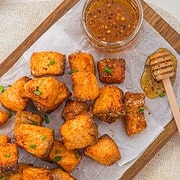 Air Fryer Parmesan Salmon Bites are served crispy on parchment with a jar of honey sauce and a honey dipper on a wooden board.