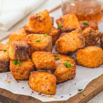 Crispy golden tofu cubes garnished with chopped chives on parchment paper, reminiscent of the delicious texture found in Air Fryer Parmesan Salmon Bites, with dipping sauce in the background.