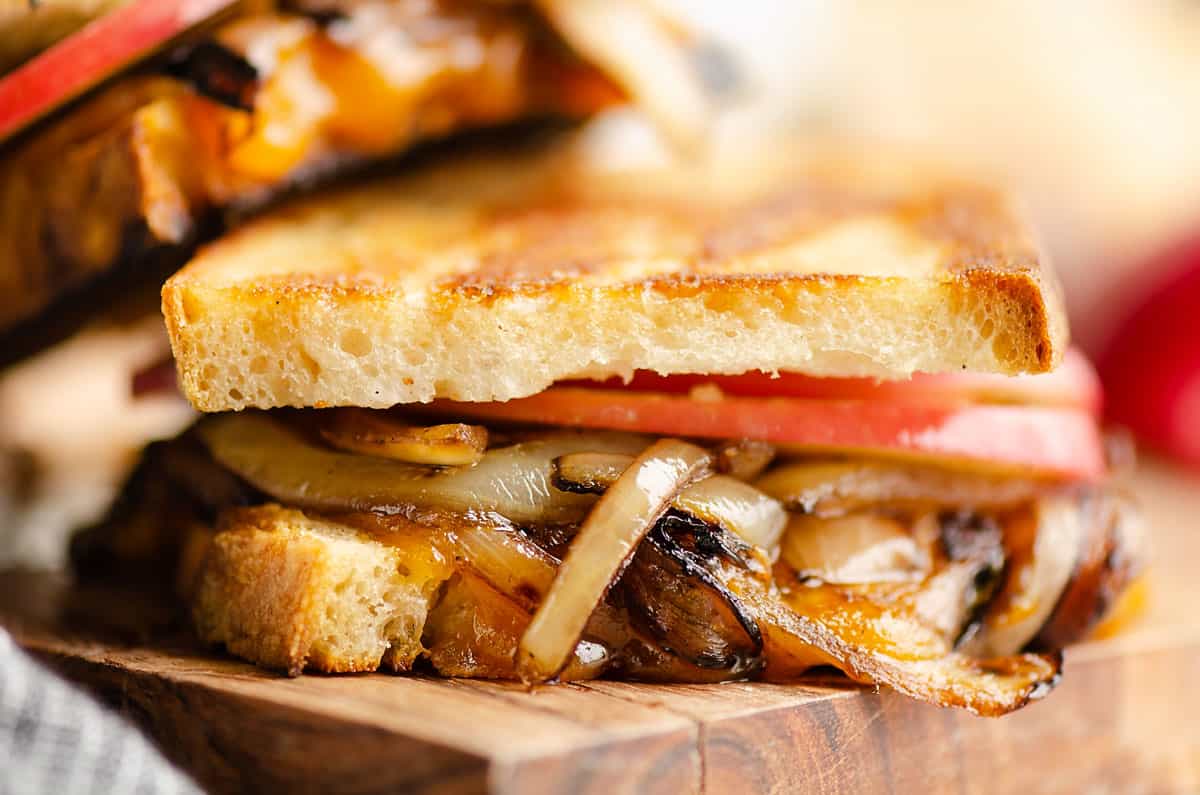 Grilled sandwich with melted cheese, saut&eacute;ed onions, and tomato slices on toasted bread, close-up.