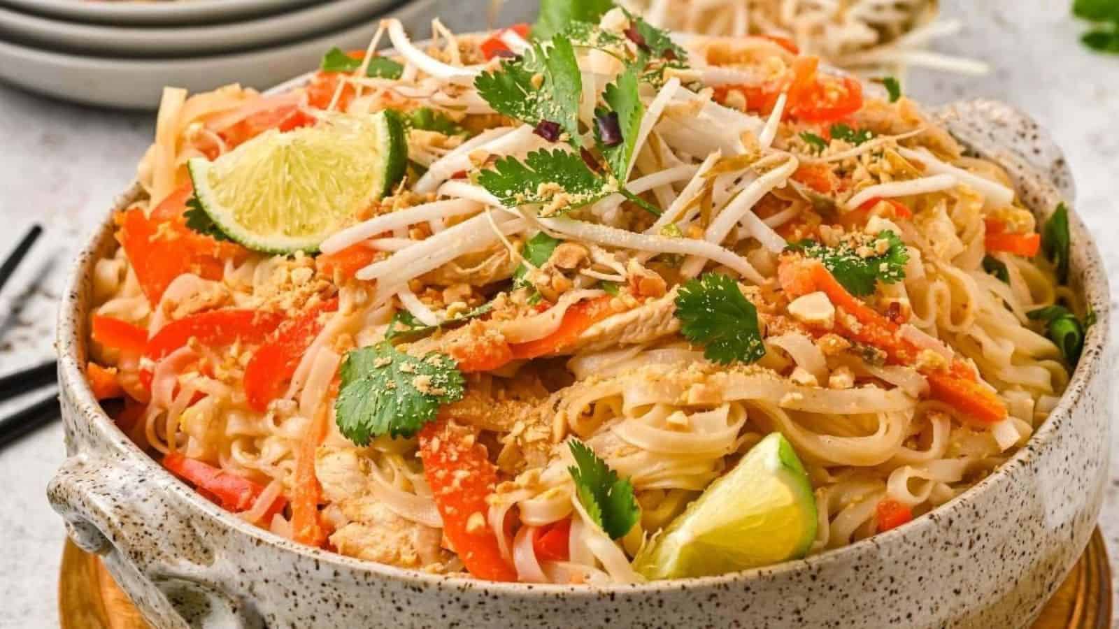 A bowl of Pad Thai noodles topped with lime, cilantro, bean sprouts, peanuts, and sliced vegetables.