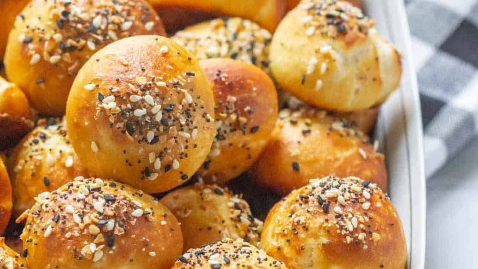 Golden-brown bread rolls topped with mixed seeds and seasoning, arranged closely together in a baking dish.