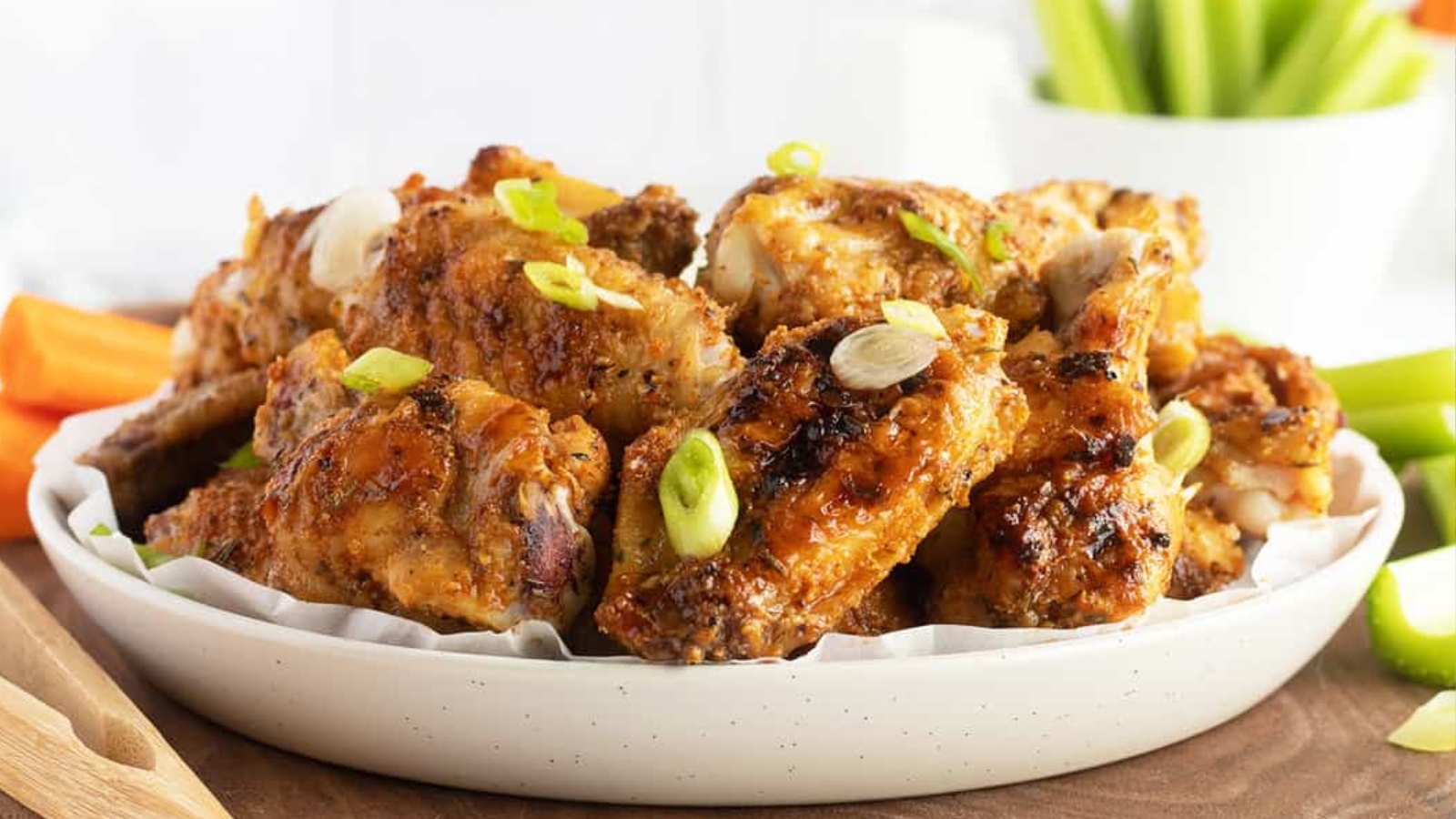 A plate of grilled chicken wings garnished with green onions, with celery and carrot sticks in the background.