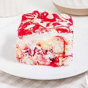 A slice of cherry dessert with whipped cream, cake layers, and almond slices on a white plate—this heaven on earth cake is a delightful treat for any occasion.