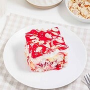 A slice of cherry dessert with almond slices on a white plate, set on a checkered tablecloth—this heavenly treat is reminiscent of a classic heaven on earth cake.