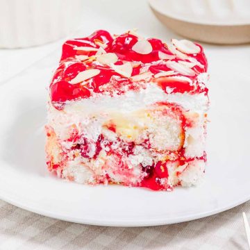 A slice of cherry dessert with whipped cream, cake layers, and almond slices on a white plate—this heaven on earth cake is a delightful treat for any occasion.