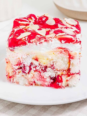 A slice of cherry dessert with whipped cream, cake layers, and almond slices on a white plate—this heaven on earth cake is a delightful treat for any occasion.