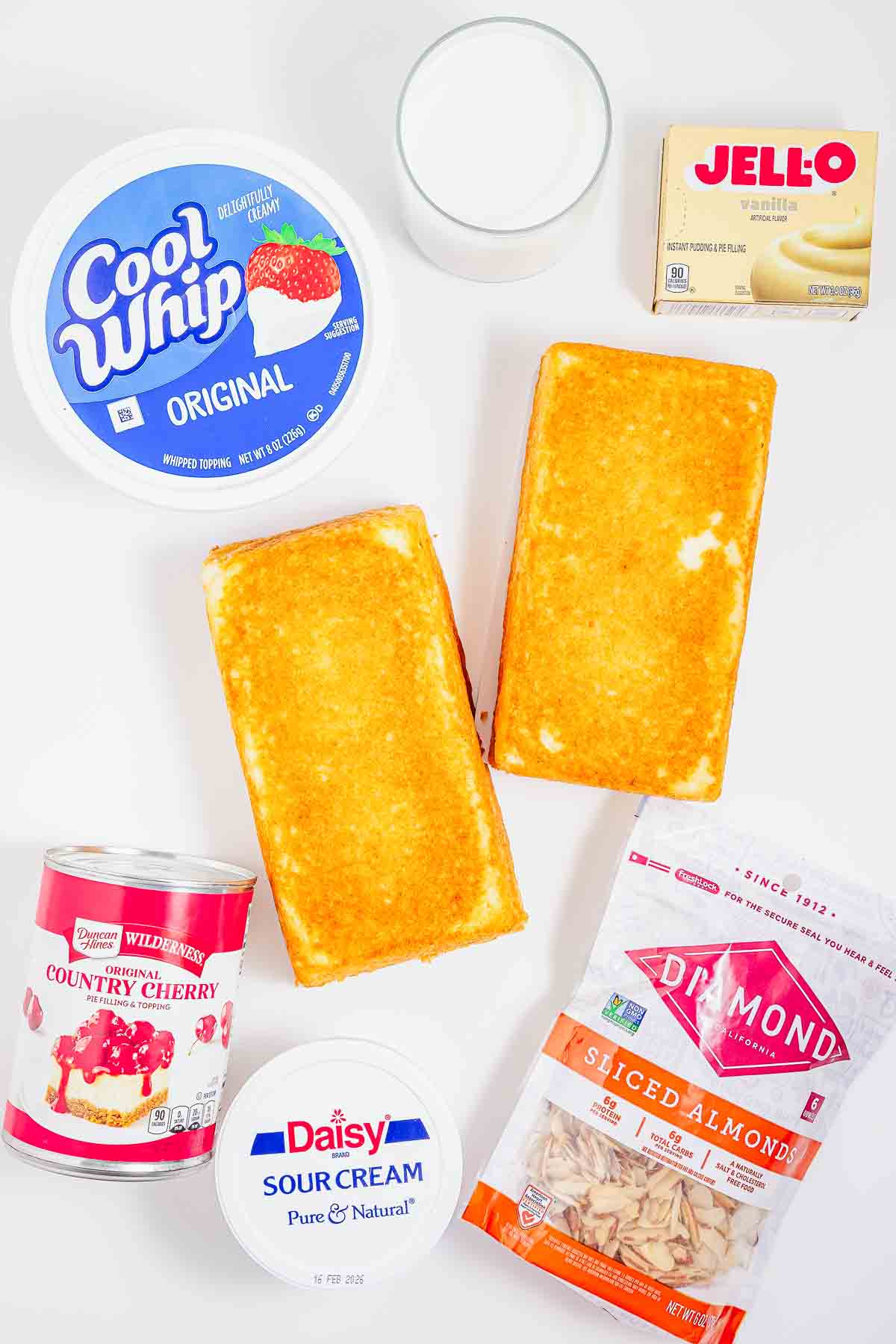 Heaven on earth cake is made with two yellow cakes, Cool Whip, milk, Jello, cherry pie filling, sour cream, and sliced almonds beautifully arranged on a white surface.