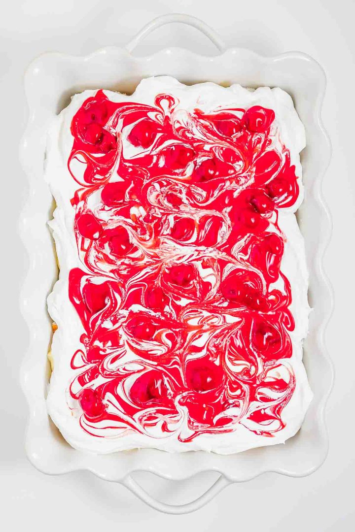 Rectangular heaven on earth cake with white frosting and bright red swirls in a white scalloped-edge baking dish.