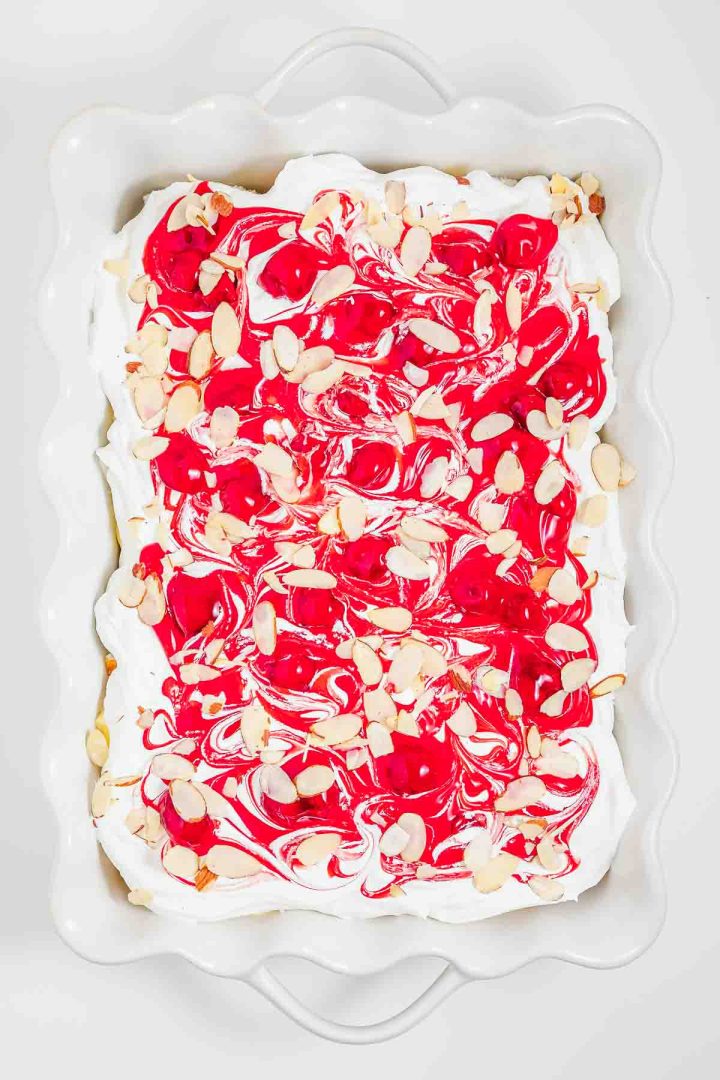 A white dish of dessert with whipped topping, red swirls, and sliced almonds on top—this heaven on earth cake is a delightful treat for any occasion.