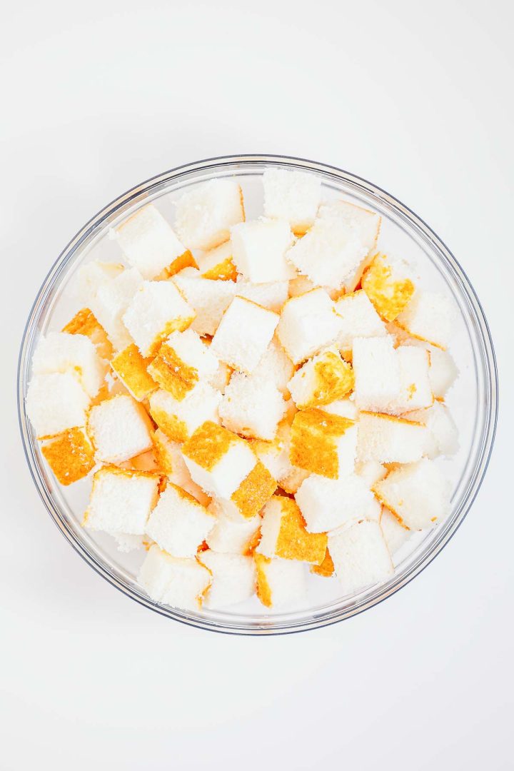 A clear bowl filled with small, cubed pieces of white and yellow heaven on earth cake sits on a white background.
