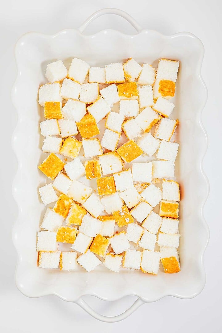 Cubed pieces of bread arranged in a white rectangular baking dish, viewed from above, ready to be transformed into a delectable heaven on earth cake.