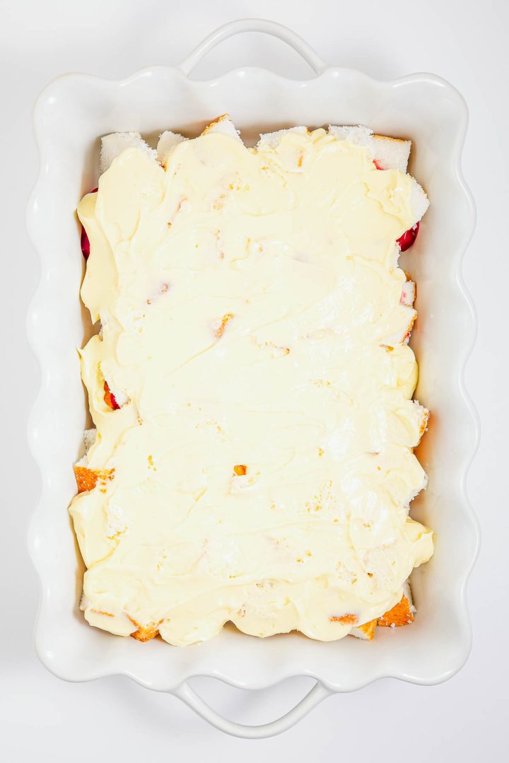 A white baking dish filled with a heaven on earth cake, its luscious layers topped with a creamy yellow mixture, seen from above.