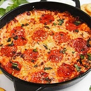 Cast iron skillet filled with baked cheesy hot honey pizza dip, topped with herbs and melted cheese.