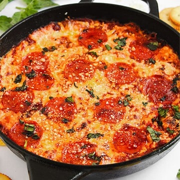 Cast iron skillet filled with baked cheesy hot honey pizza dip, topped with herbs and melted cheese.