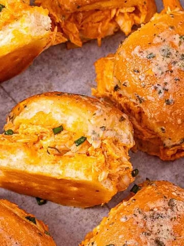 Buffalo chicken sliders with shredded filling on soft buns, topped with herbs and arranged on a surface—this easy sliders recipe is perfect for any gathering.