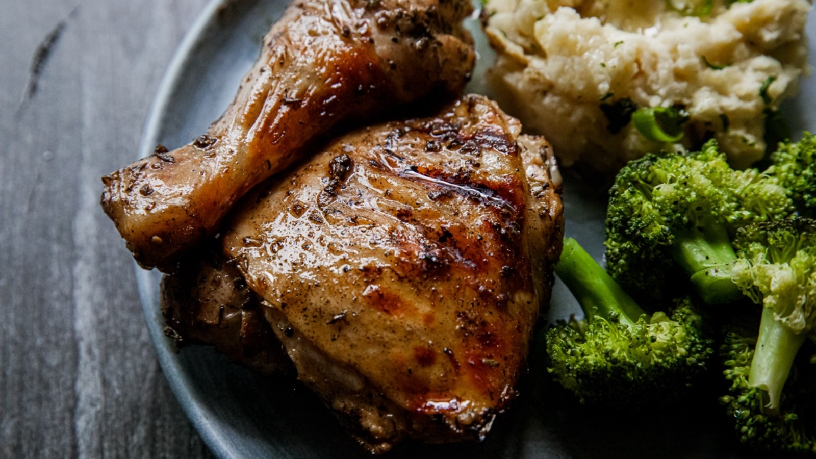 Roast chicken with mashed potatoes and broccoli on a plate, shot up close on a rustic surface.