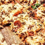Sliced pizza on a wooden board, topped with pepperoni, Italian sausage, melted cheese, and herbs—just like a classic Italian Sausage Sheet Pan Pizza.