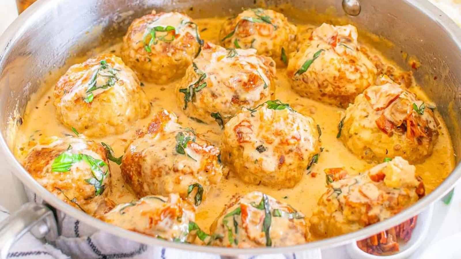 Meatballs simmering in a creamy sauce, garnished with chopped herbs in a stainless steel pan&mdash;perfect for adding to your collection of World-Inspired Chicken Dinners.