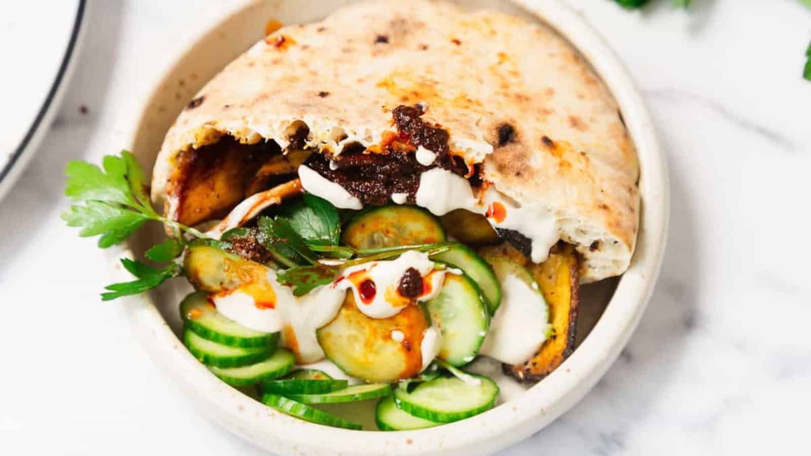 Pita stuffed with cucumbers, roasted vegetables, parsley, and drizzled with white and red sauces.