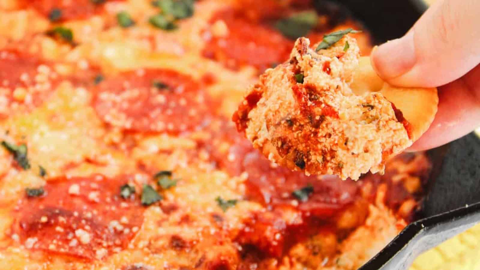 Cast iron skillet pizza with pepperoni, melted cheese, herbs, and crackers on the side, viewed from above.