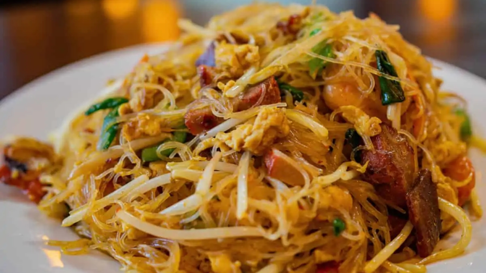 Rice noodles with meat and veggies on a white plate.