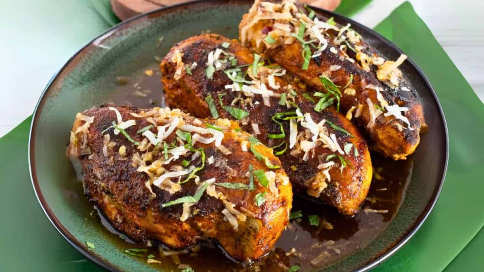 Three seasoned chicken breasts topped with shredded cheese and herbs on a dark plate with green garnishes.