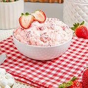 A bowl of pink strawberry fluff dessert topped with sliced strawberries sits on a red checkered cloth.