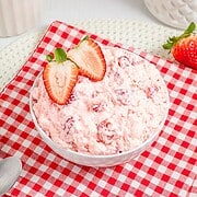 A bowl of Strawberry Fluff salad with sliced strawberries on top, placed on a red checkered cloth.