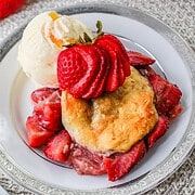 Vanilla ice cream with Strawberry Shortcake Casserole and sliced strawberries on a white plate with a silver rim.