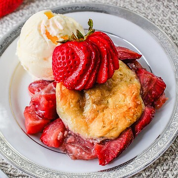Vanilla ice cream with Strawberry Shortcake Casserole and sliced strawberries on a white plate with a silver rim.