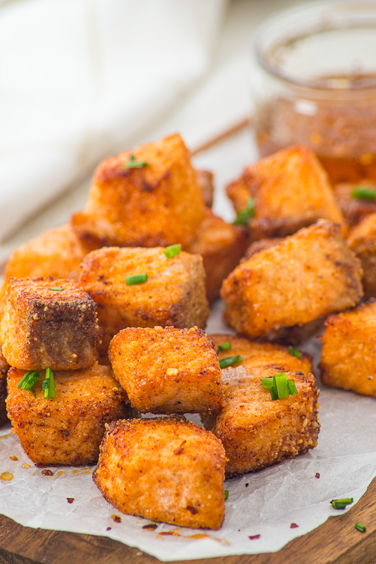 Crispy, golden-brown tofu cubes garnished with green herbs, served on parchment with dipping sauce in the background—perfect for pairing with Air Fryer Parmesan Salmon Bites for a deliciously satisfying spread.