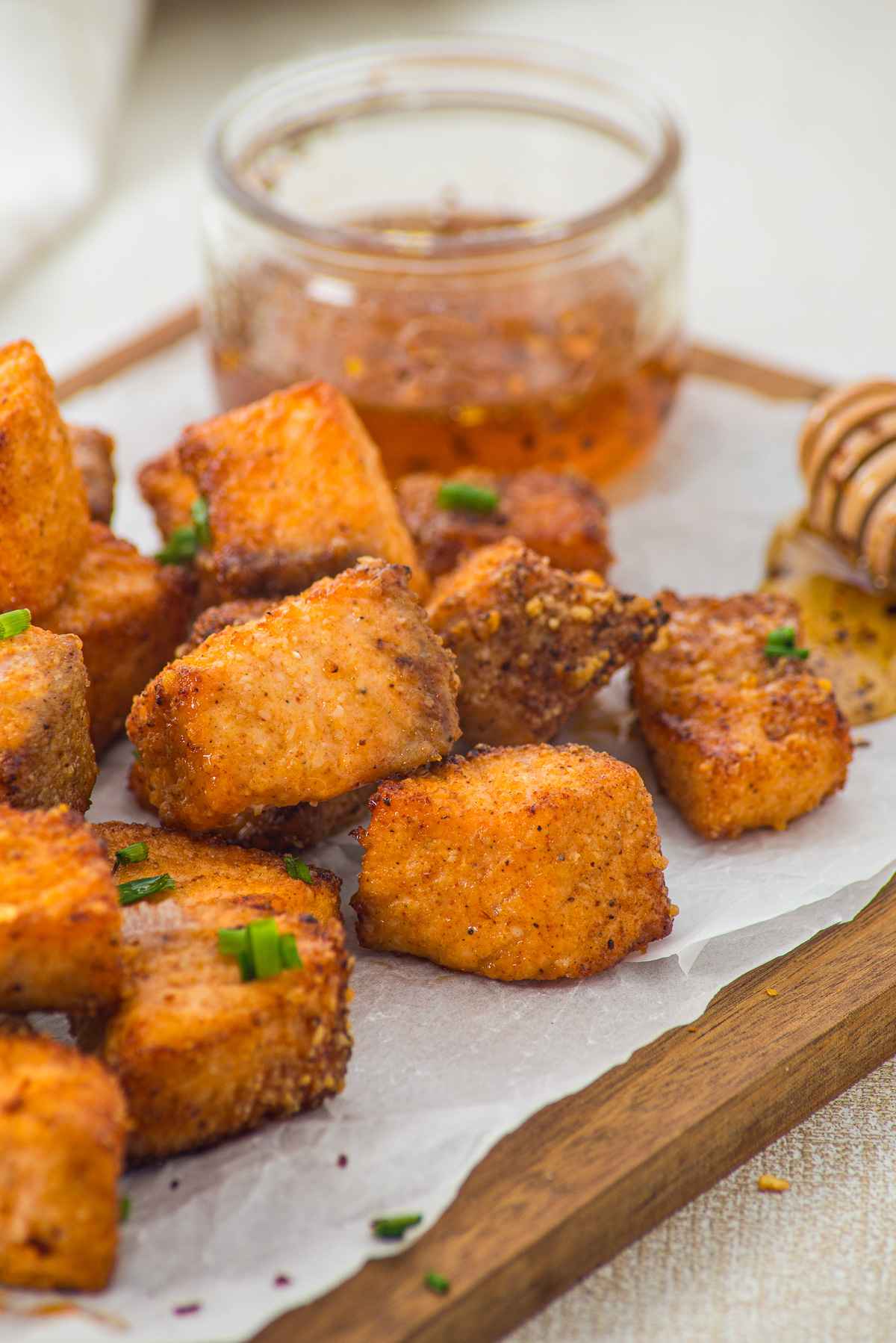 Crispy fried chicken bites on parchment with a jar of honey dipping sauce and a honey dipper nearby, reminiscent of the irresistible crunch found in Air Fryer Parmesan Salmon Bites.